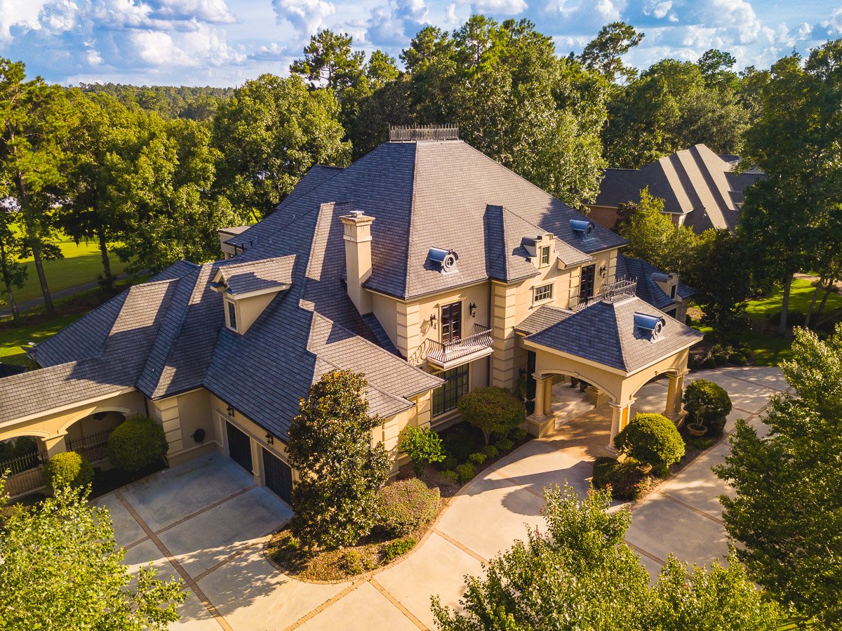 Professional aerial real estate photography of a luxury estate with grand architecture, landscaped grounds, and a sweeping circular driveway.