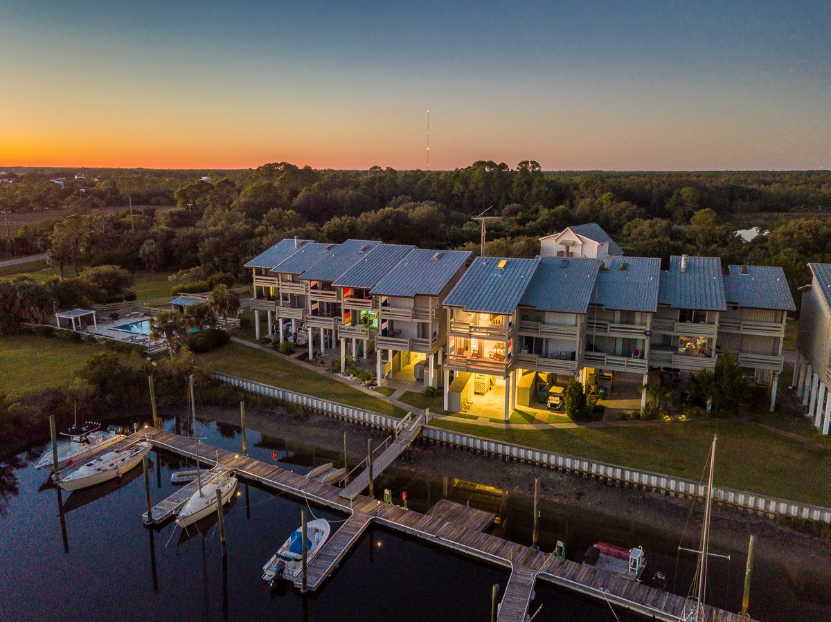 Professional aerial real estate photography of waterfront townhomes and a private marina at sunset, showcasing docks, boats, and scenic coastal views.