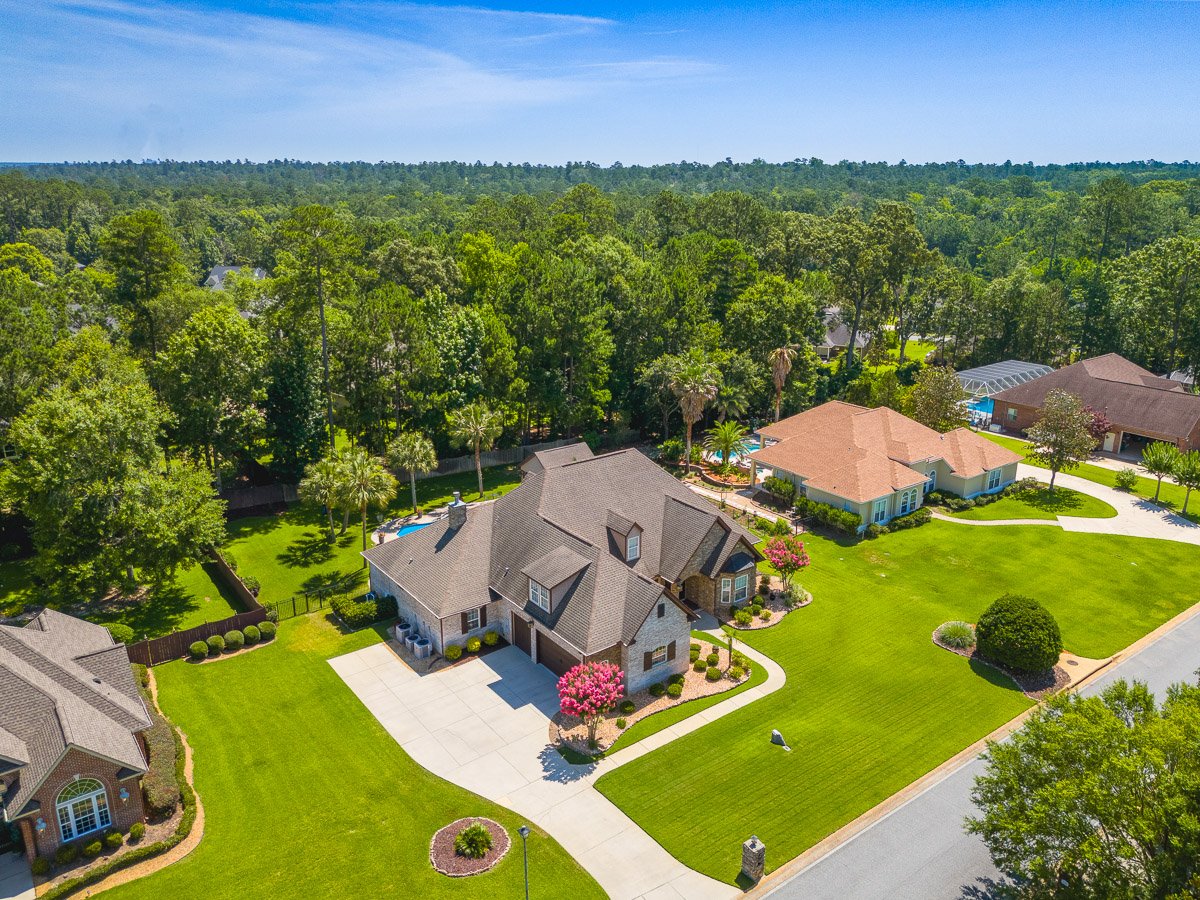 Professional aerial real estate photography of a luxury residential neighborhood with large homes, manicured lawns, mature trees, and spacious lots.