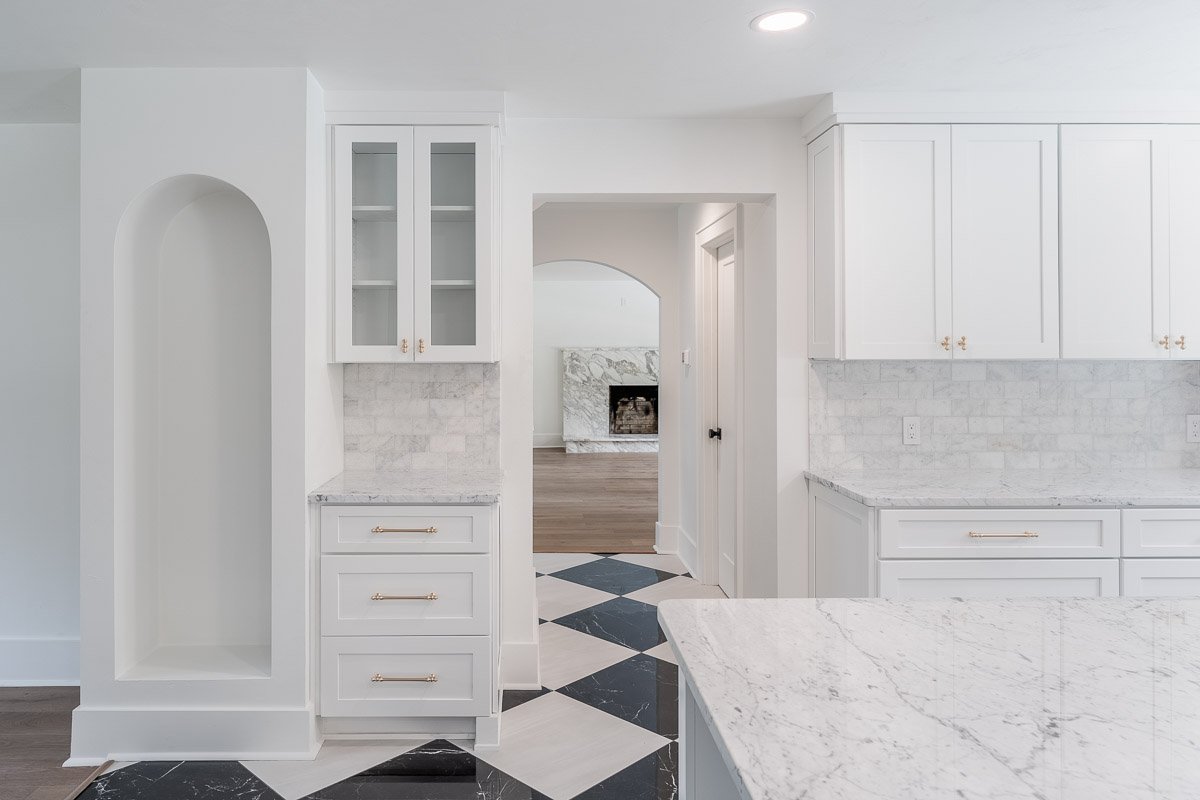 Professional real estate photography of a luxury Seattle kitchen with white cabinetry, marble countertops, brass hardware, black-and-white tile flooring, and elegant architectural details.