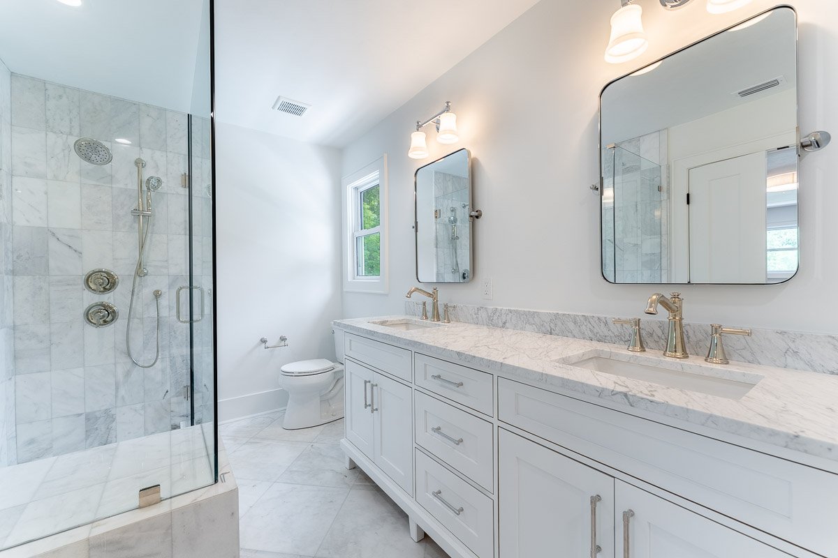 Professional real estate photography of a luxury Seattle bathroom with a marble walk-in shower, double vanity, polished fixtures, and bright modern finishes.