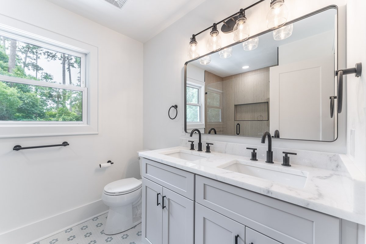 Professional real estate photography of a modern Seattle bathroom with a double vanity, marble countertop, black fixtures, oversized mirror, and bright natural light.