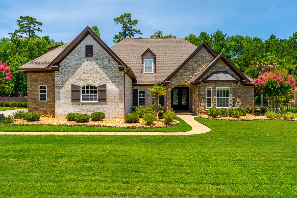Professional real estate exterior photography of a luxury home with stone and brick details, manicured landscaping, and strong curb appeal.