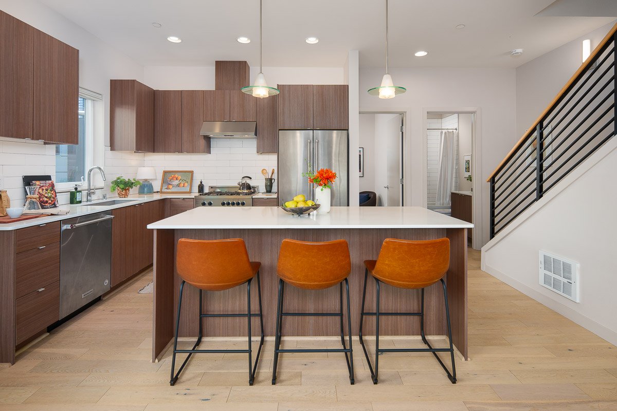 Professional flambient real estate photography of a modern Seattle townhouse kitchen with wood cabinetry, large island, stainless steel appliances, and contemporary finishes.