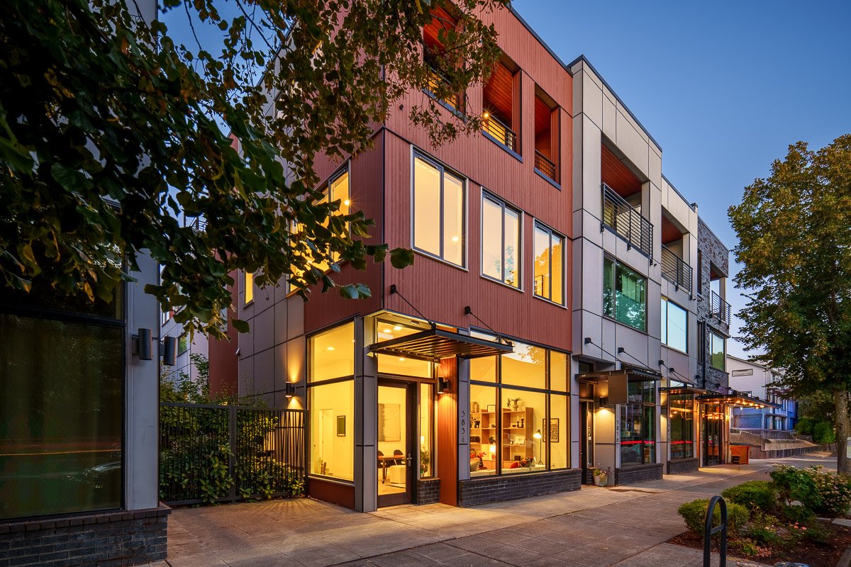 Professional real estate photography of a modern Seattle live-work building at dusk with street-level commercial space, contemporary architecture, and warm interior lighting.