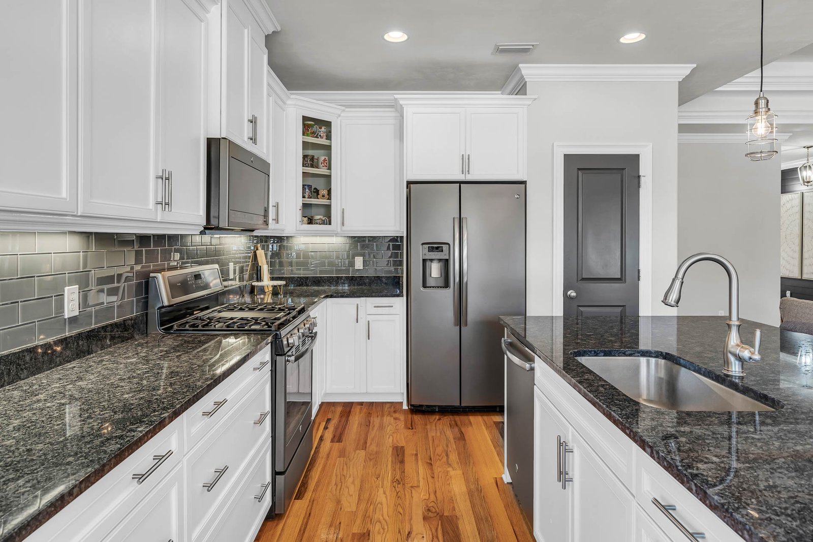 Professional real estate photography of a modern Seattle kitchen with white cabinetry, dark granite countertops, stainless steel appliances, and hardwood floors.