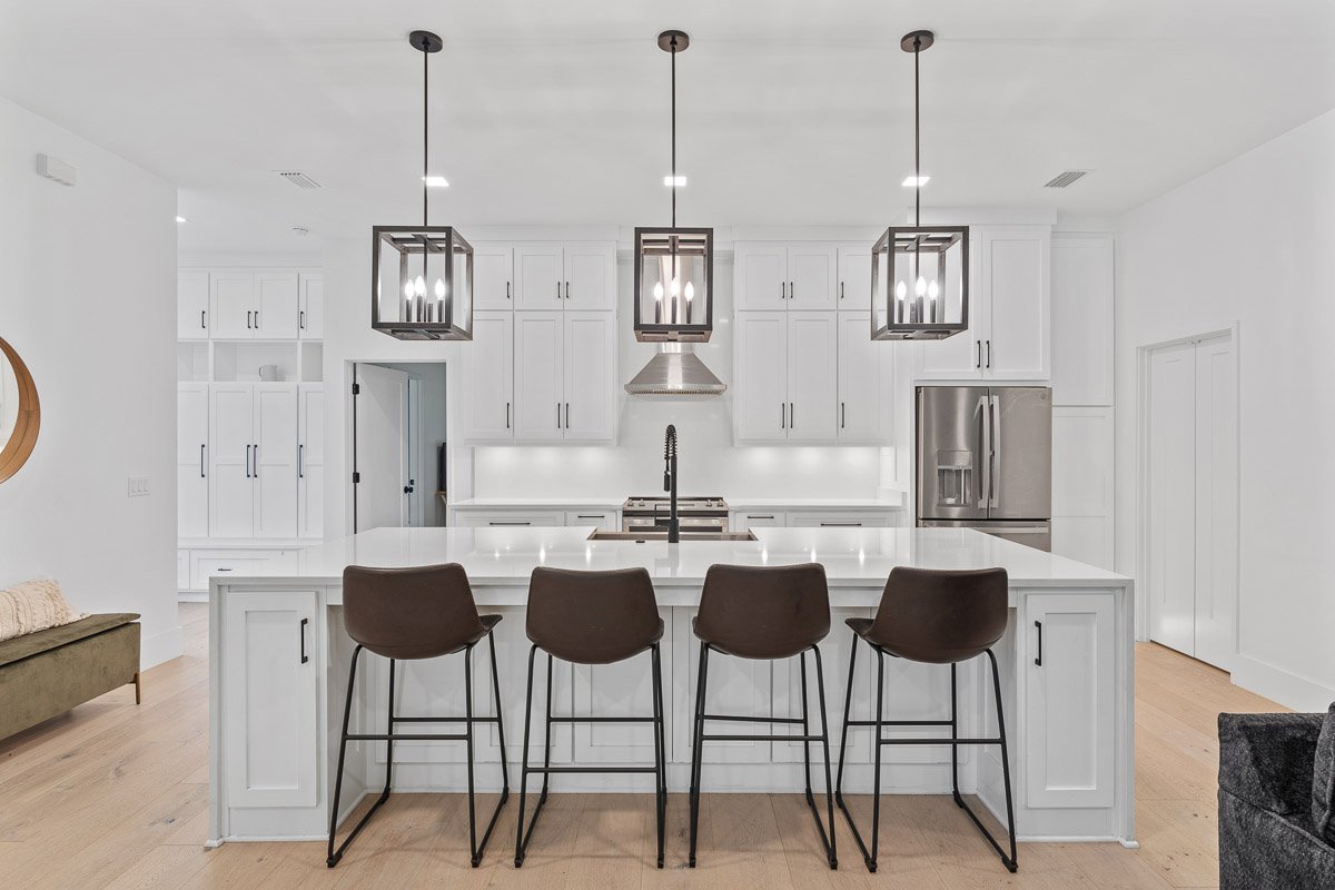 Professional real estate photography of a modern Seattle kitchen with white cabinetry, oversized island, pendant lighting, stainless steel appliances, and contemporary finishes.