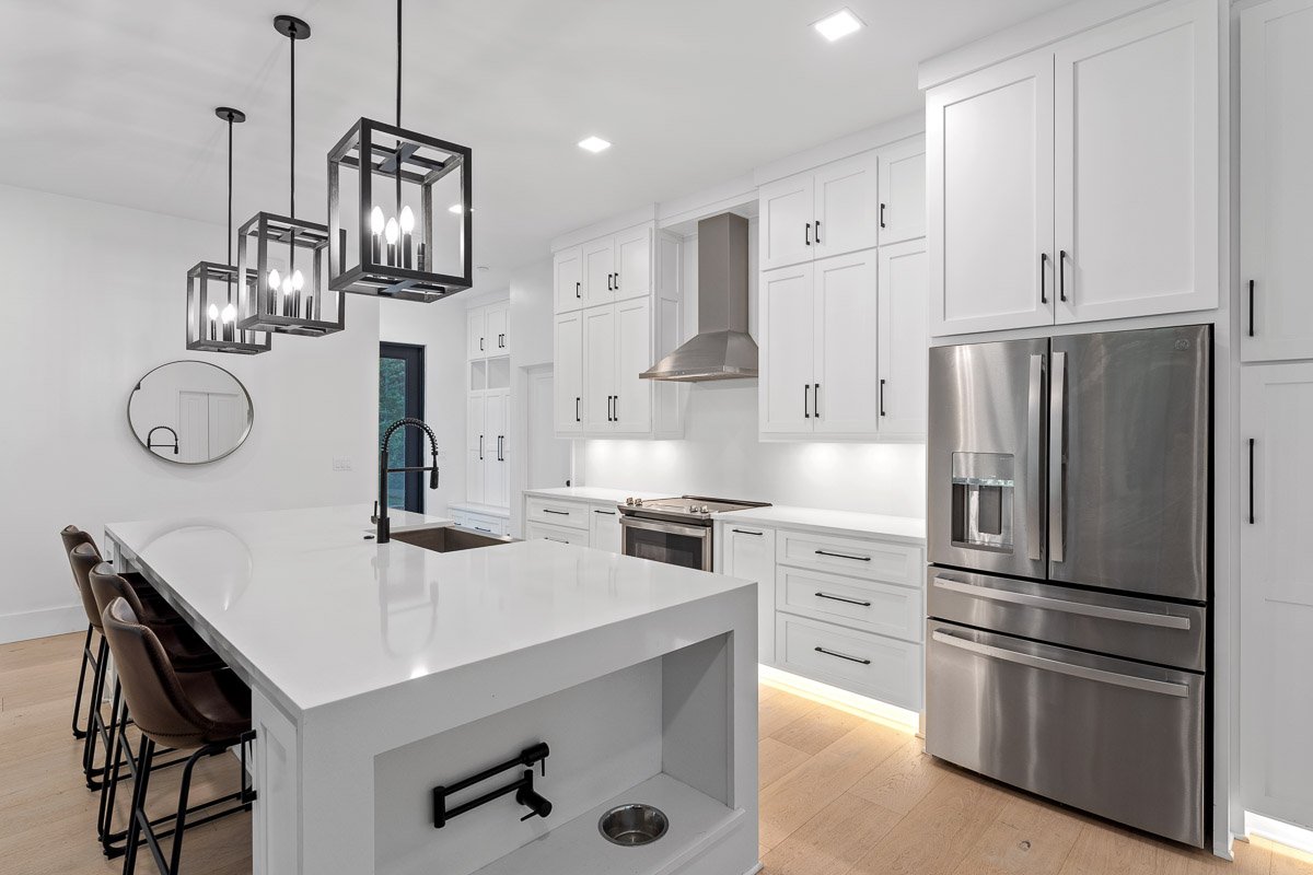 Professional real estate photography of a luxury Seattle kitchen with white cabinetry, oversized waterfall island, statement pendant lighting, stainless steel appliances, and modern black accents.