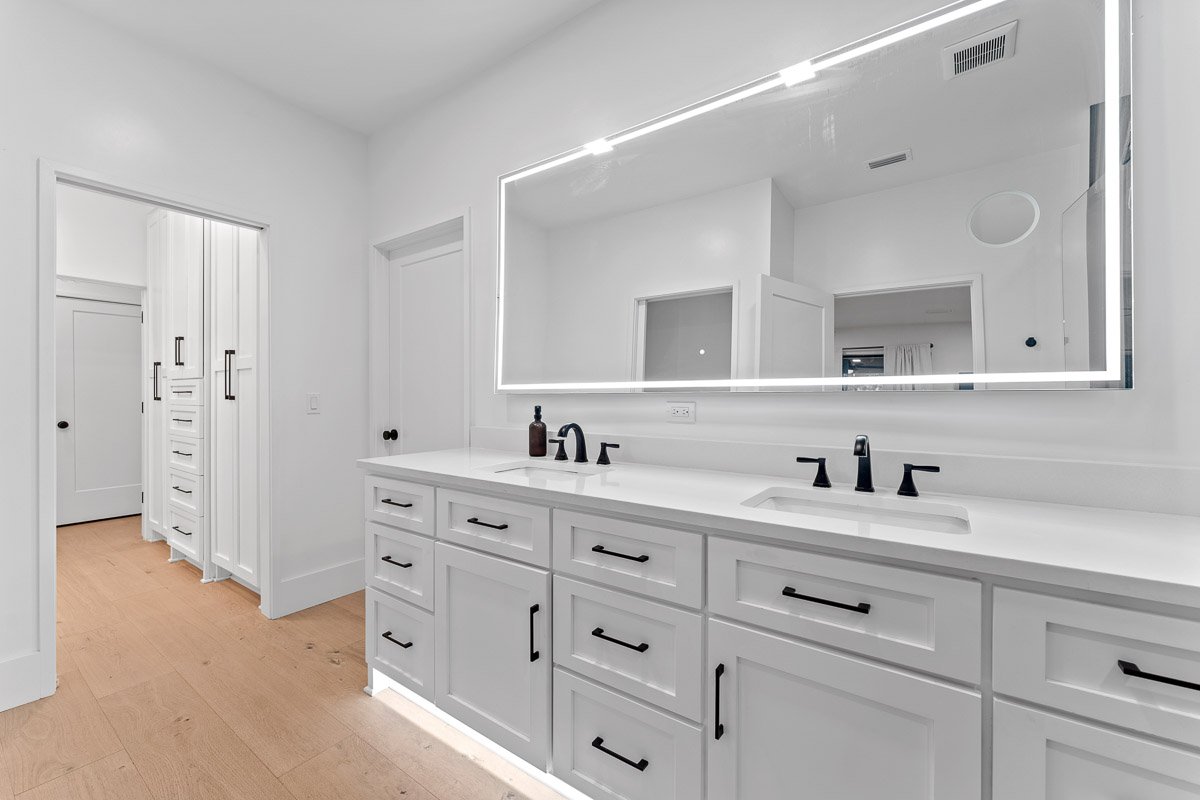 Professional real estate photography of a luxury Seattle primary bathroom with a double vanity, illuminated mirror, modern black fixtures, and adjoining walk-in closet.