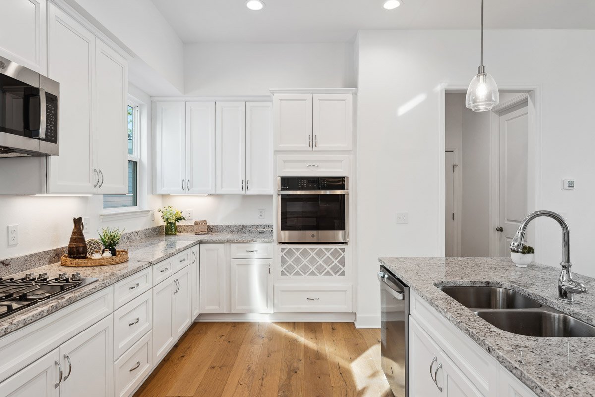 Professional real estate photography of a bright Seattle kitchen with white cabinetry, granite countertops, stainless steel appliances, a center island, and hardwood floors.