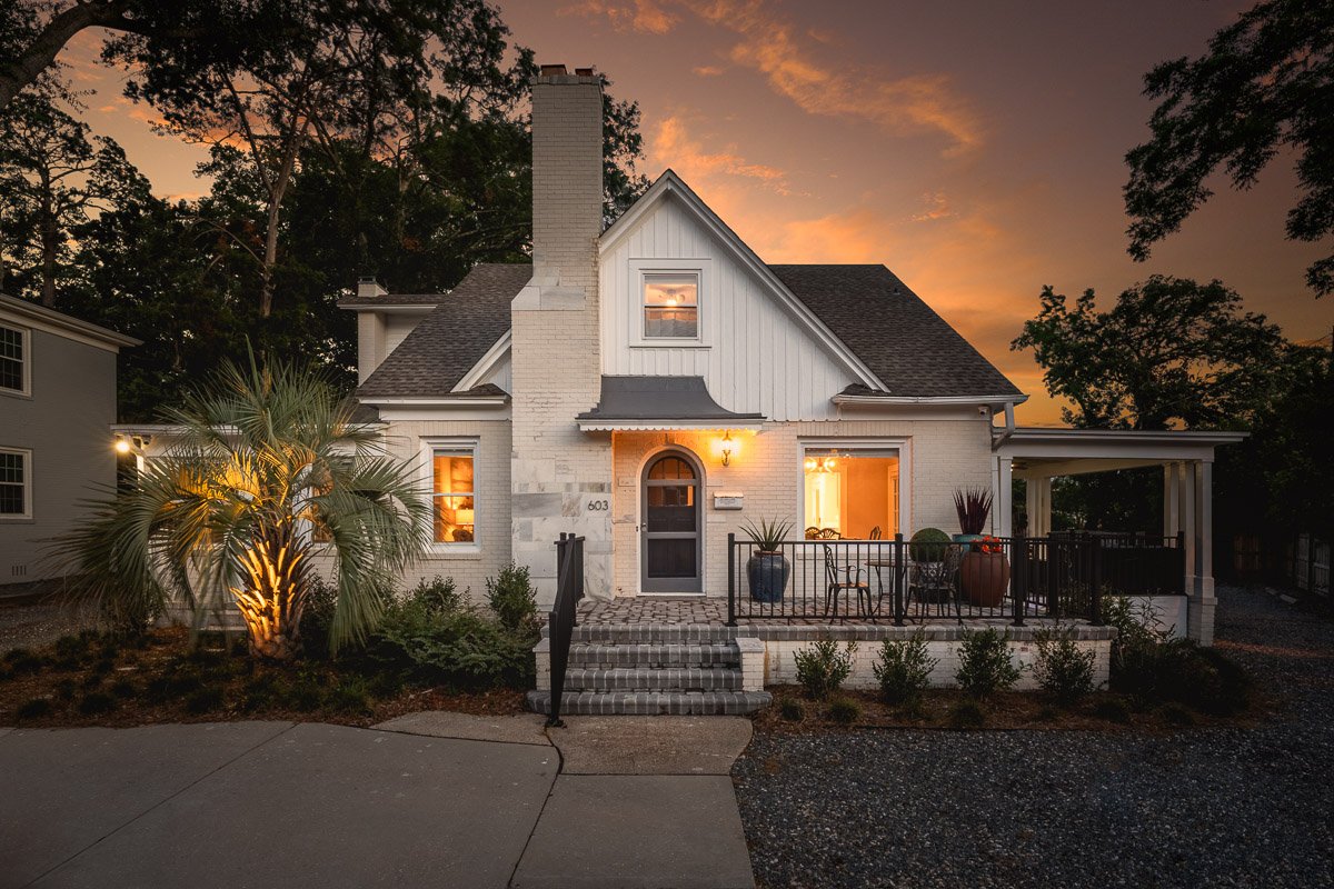 Professional twilight real estate photography of a charming home exterior with warm interior lighting, landscaped curb appeal, and a dramatic sunset sky.
