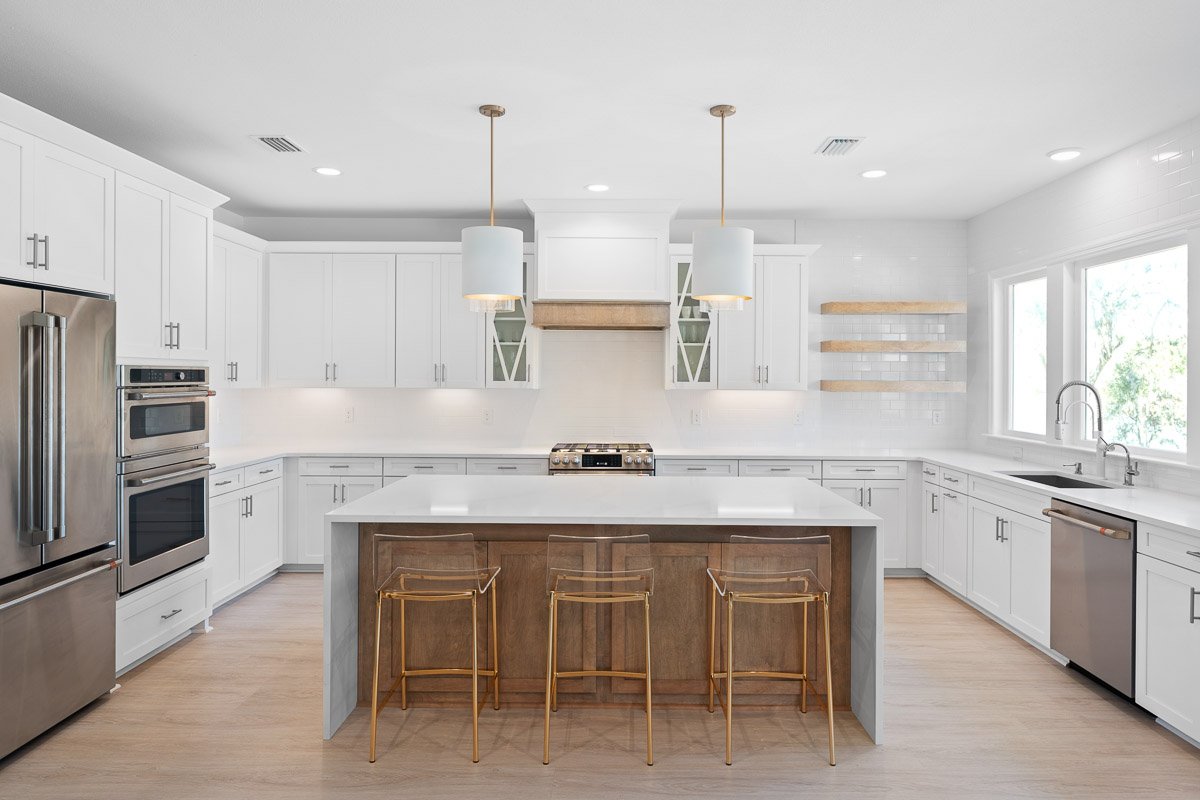 Professional real estate photography of a bright luxury Seattle kitchen with white cabinetry, oversized island, pendant lighting, stainless steel appliances, and modern finishes.