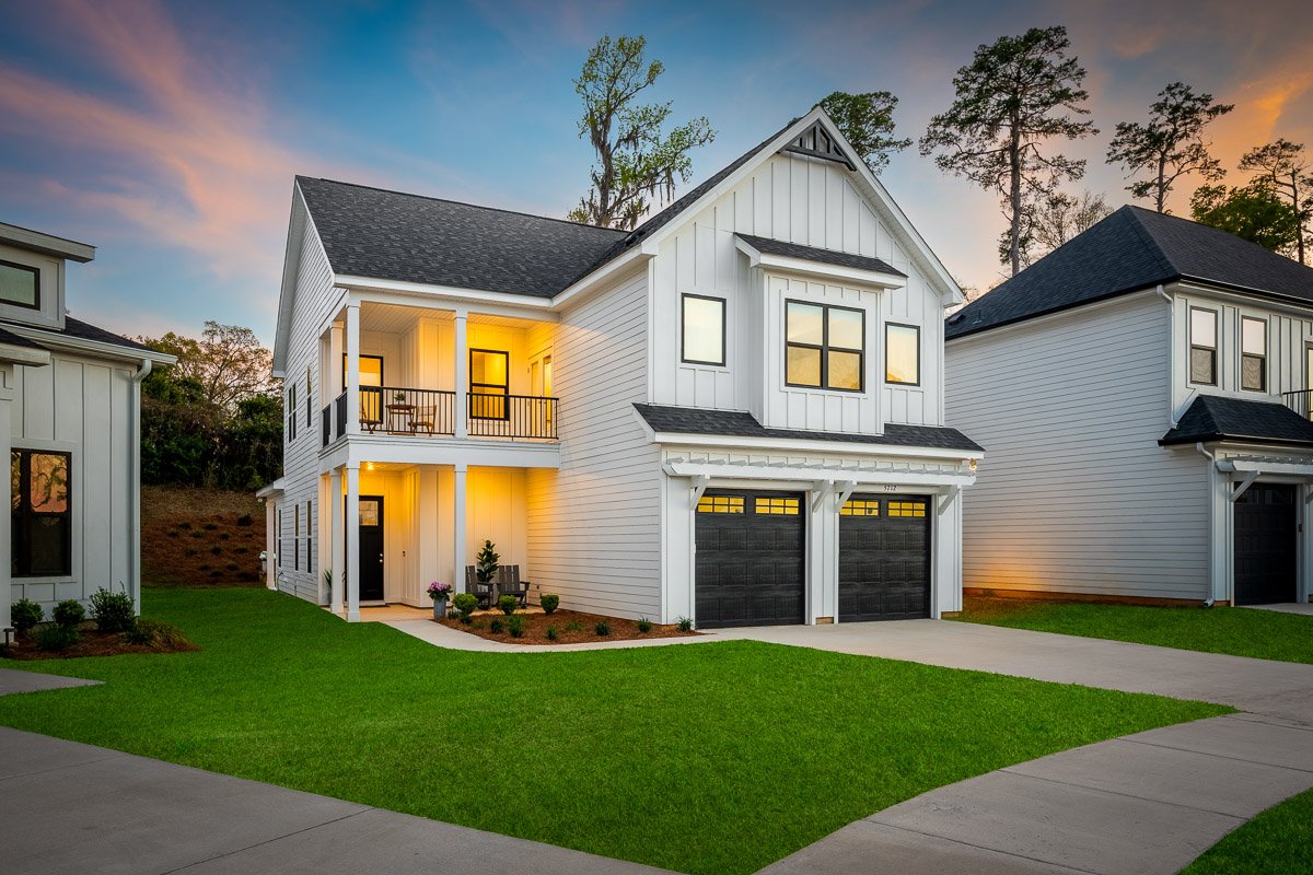 Professional twilight real estate photography of a modern Seattle home with farmhouse-inspired architecture, warm exterior lighting, a covered balcony, and strong curb appeal.
