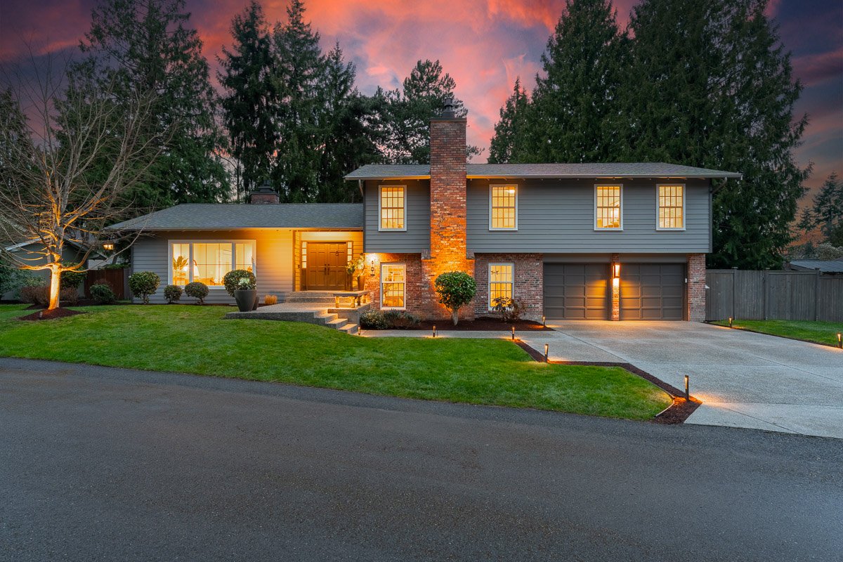 Professional twilight real estate photography of a Mercer Island home with warm interior lighting, manicured landscaping, mature trees, and dramatic sunset skies.