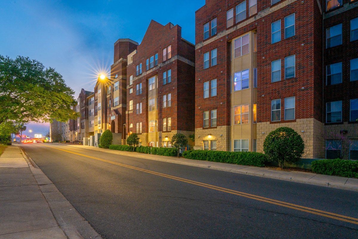Professional real estate photography of student apartment buildings at dusk, showcasing multi-family housing, brick architecture, and a well-lit urban streetscape.