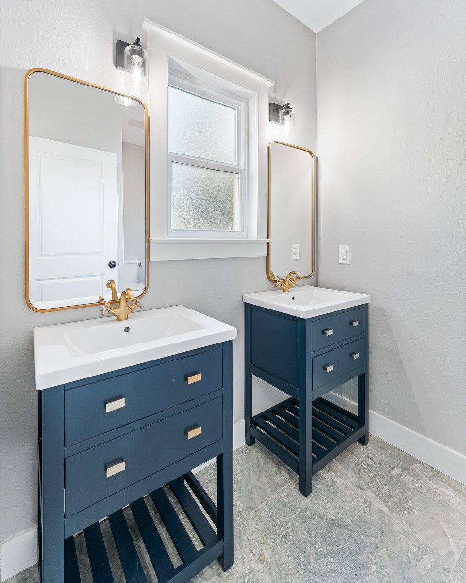 Professional real estate photography of a stylish Seattle bathroom with dual navy vanities, gold fixtures, modern mirrors, and bright contemporary finishes.