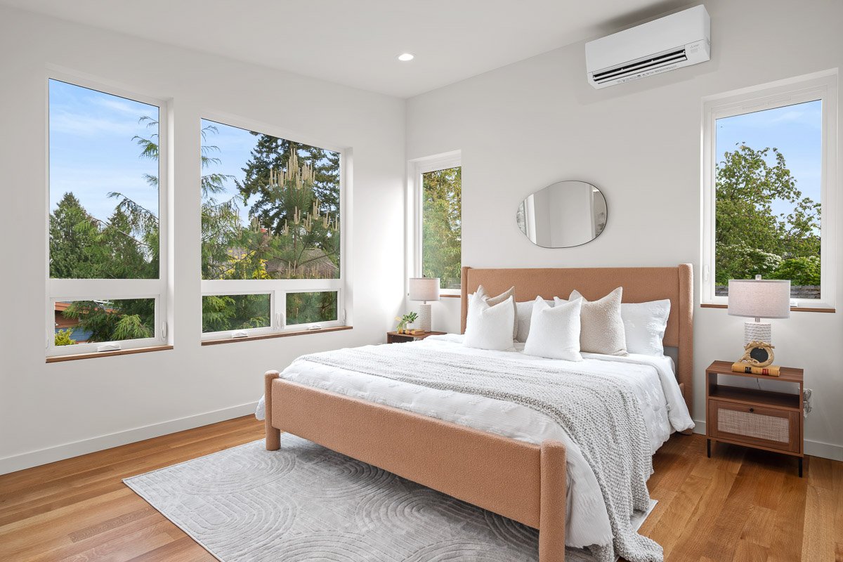 Professional real estate photography of a bright Seattle primary bedroom with large windows, modern staging, hardwood floors, and abundant natural light.