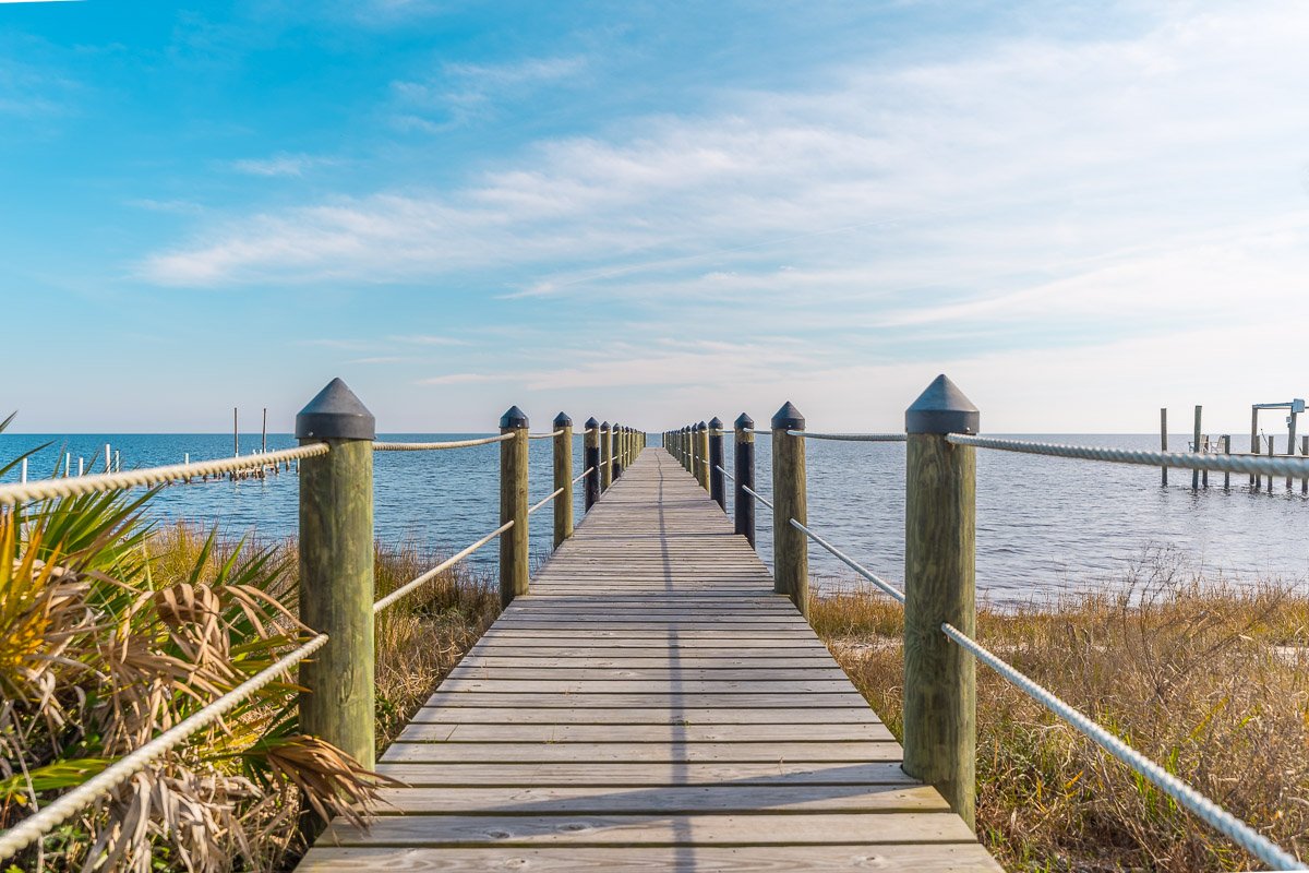 Professional waterfront real estate photography of a private wooden pier extending into calm blue water, showcasing expansive views and coastal lifestyle appeal.