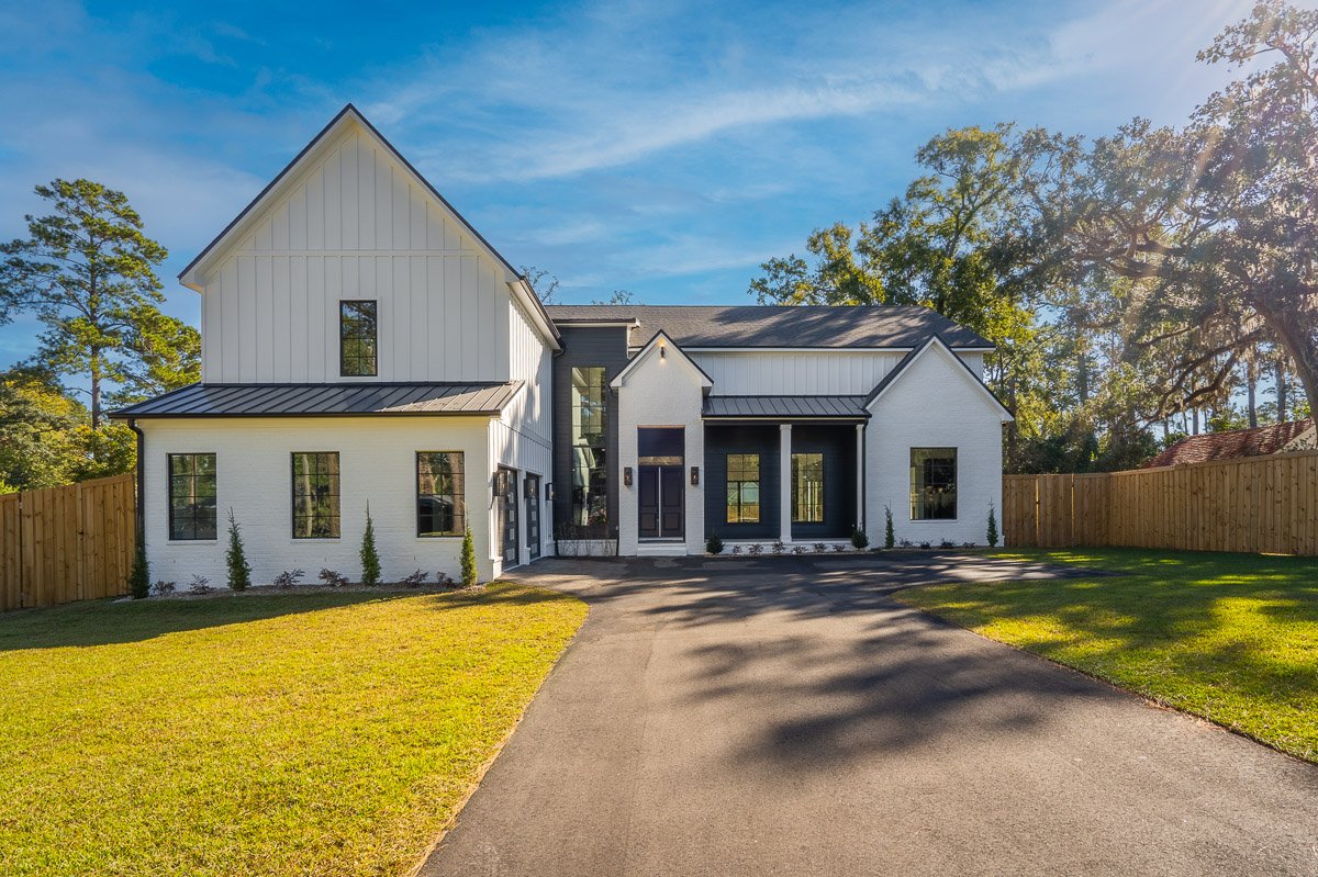 Professional real estate exterior photography of a luxury modern farmhouse-style home with white brick, black accents, a circular driveway, and mature landscaping.