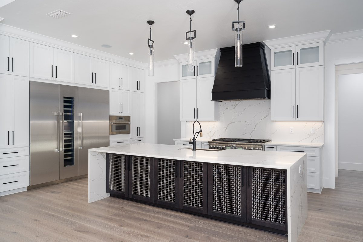 Professional flambient real estate photography of a luxury Seattle kitchen with white cabinetry, waterfall island, black range hood, stainless steel appliances, and modern pendant lighting.