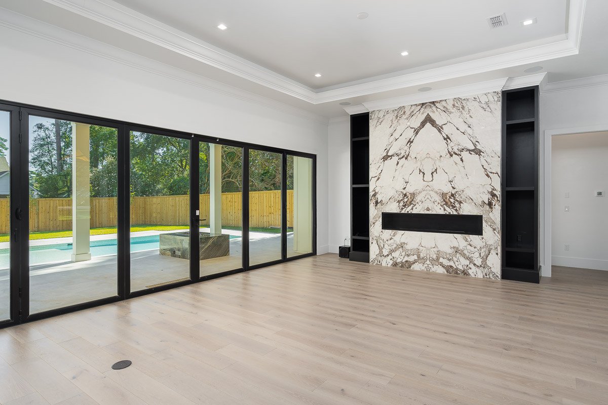 Professional real estate photography of a luxury Seattle living room with a dramatic bookmatched stone fireplace, floor-to-ceiling sliding glass doors, light wood floors, and views of the backyard pool.