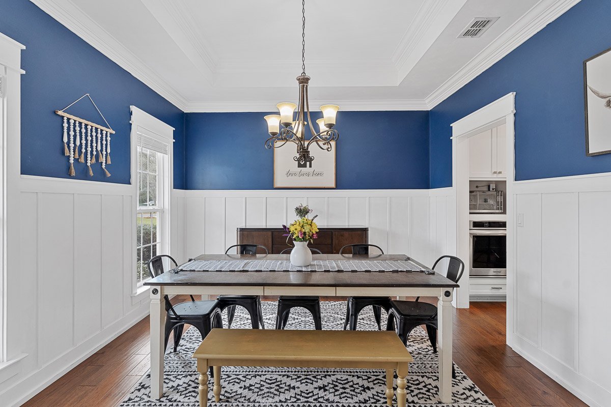 Professional real estate photography of a stylish Seattle dining room with blue accent walls, white wainscoting, hardwood floors, and traditional chandelier lighting.