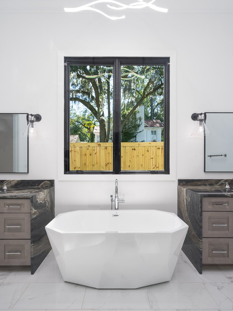 Professional flambient real estate photography of a luxury Seattle bathroom with a freestanding soaking tub, dual vanities, large window, and dramatic stone finishes.