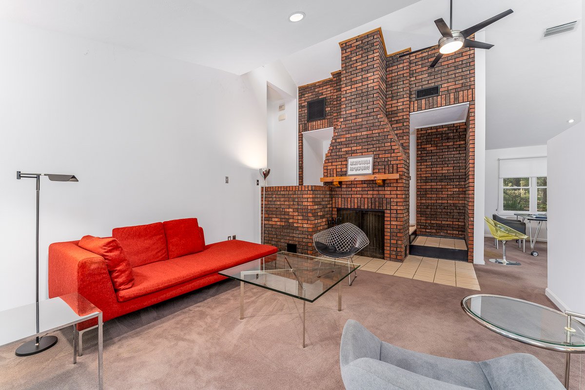 Professional flambient real estate photography of a contemporary Seattle living room with a dramatic brick fireplace, vaulted ceiling, modern furnishings, and open layout.