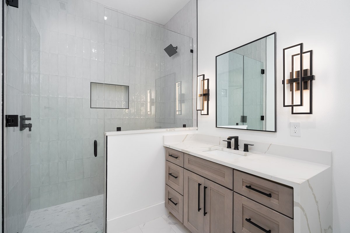 Professional real estate photography of a modern Seattle bathroom with a glass walk-in shower, floating vanity, quartz countertop, black fixtures, and contemporary lighting.