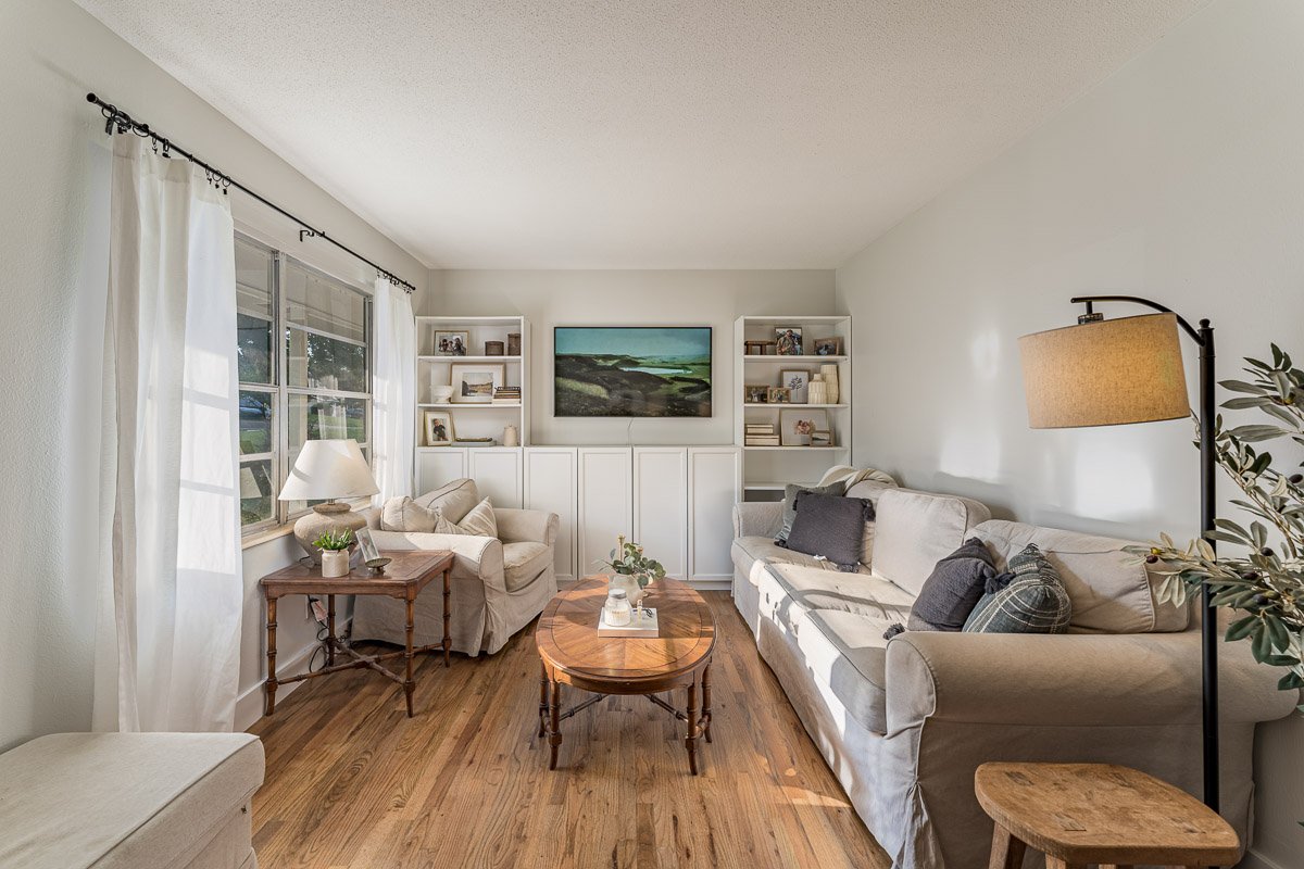 Professional real estate photography of a cozy staged living room with neutral furnishings, built-in shelving, hardwood floors, and soft flambient lighting.