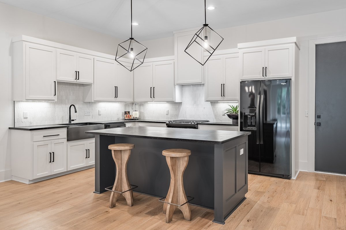 Professional real estate photography of a modern Seattle townhouse kitchen with white cabinetry, black island, pendant lighting, and hardwood floors.