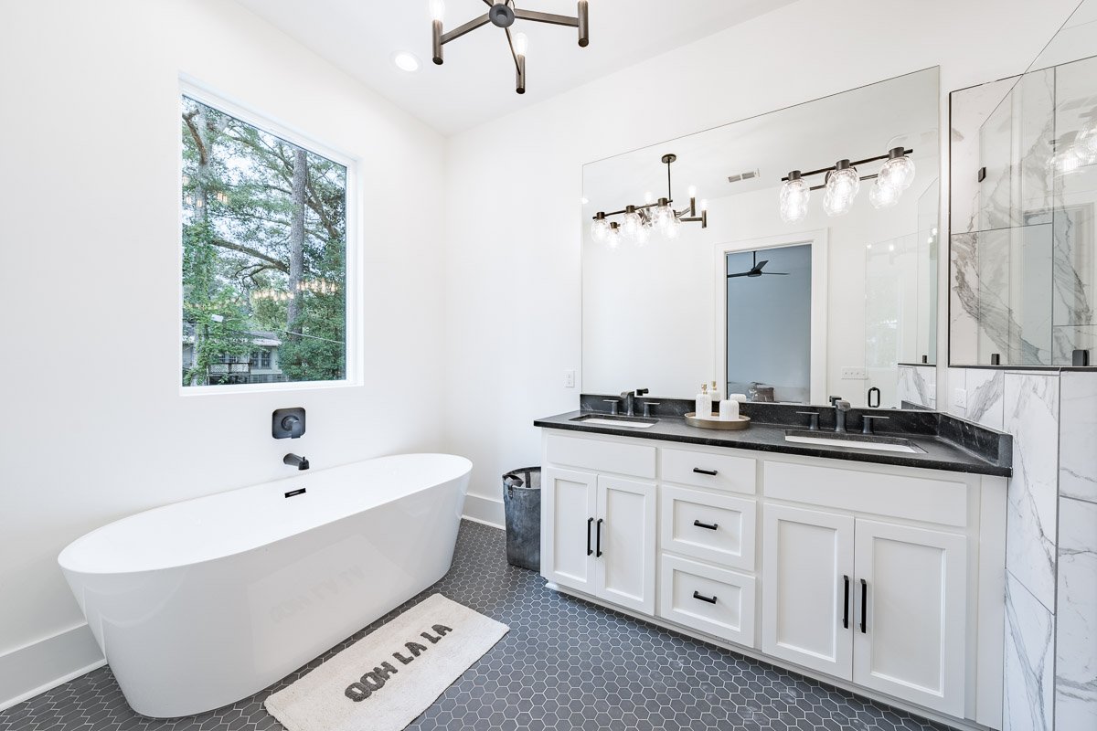 Professional real estate photography of a luxury Seattle bathroom with a freestanding soaking tub, double vanity, oversized mirror, marble shower, and modern black fixtures.