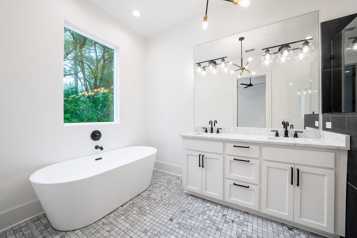 Professional real estate photography of a luxury Seattle bathroom with a freestanding soaking tub, double vanity, marble countertop, oversized mirror, and modern black fixtures.