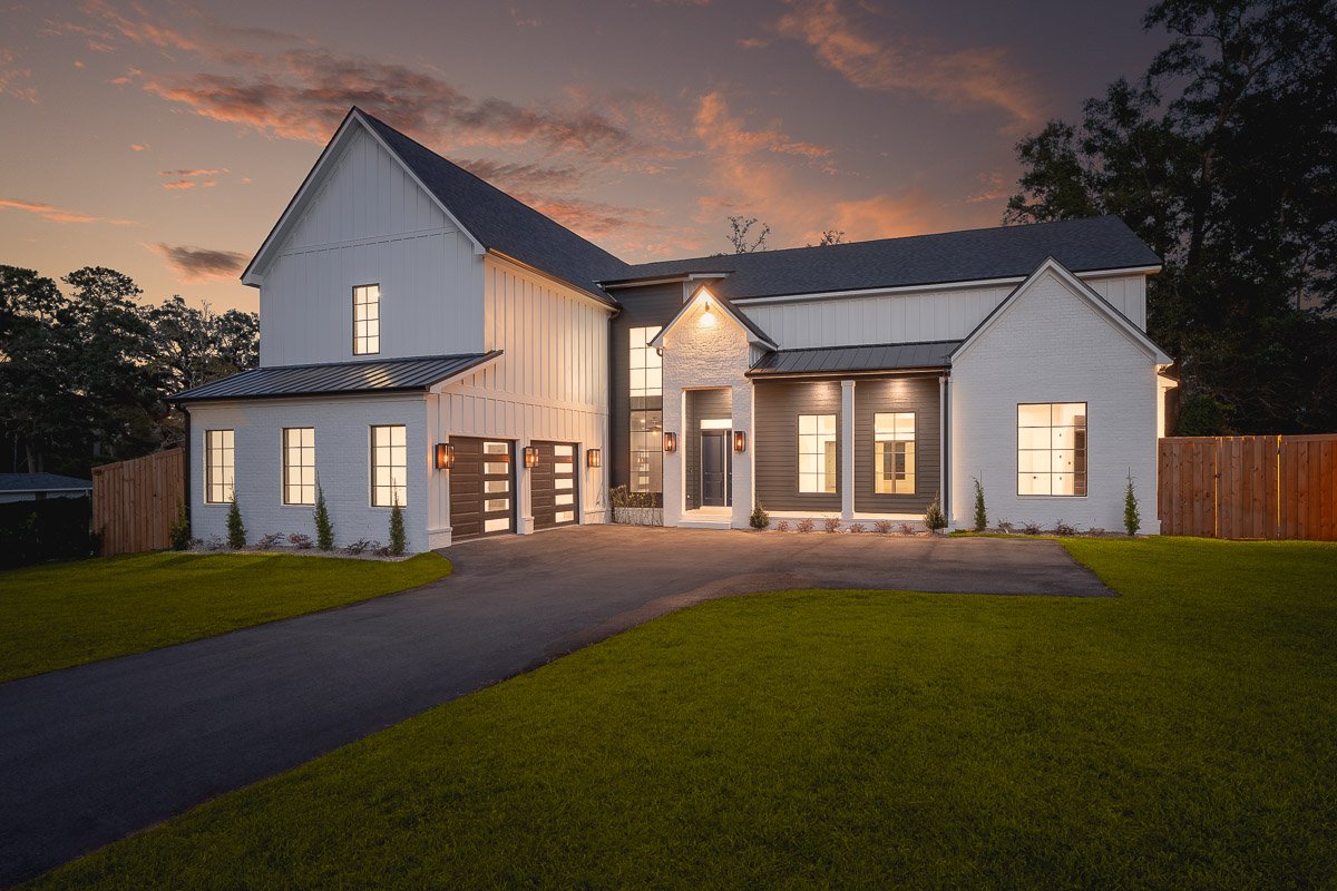 Professional twilight real estate photography of a luxury modern farmhouse-style home with warm interior lighting, black accents, manicured lawn, and dramatic sunset skies.