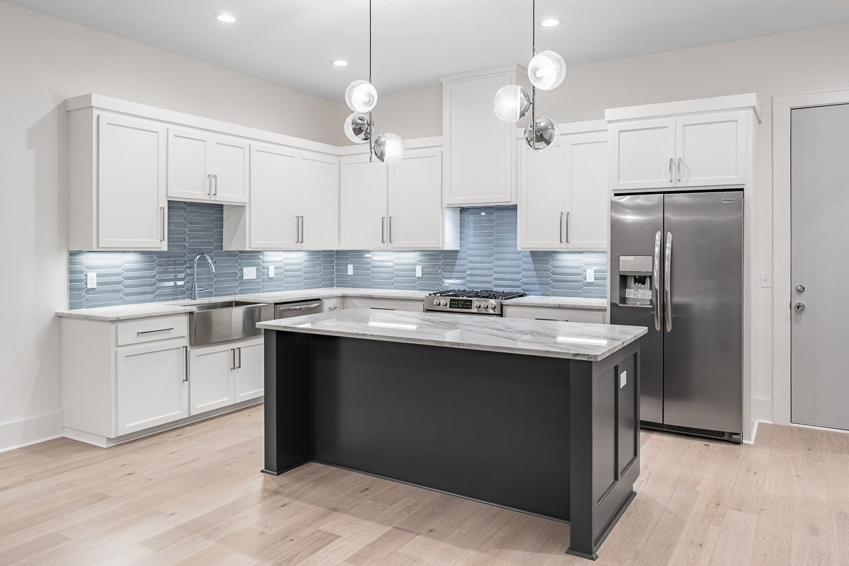 Professional real estate photography of a modern Seattle kitchen with white cabinetry, black island, marble countertops, stainless steel appliances, blue tile backsplash, and contemporary pendant lighting.