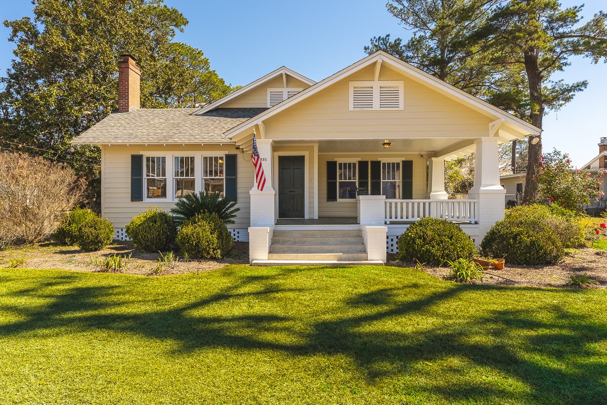 Professional real estate photography of a charming bungalow-style home with a covered front porch, mature landscaping, and inviting curb appeal.