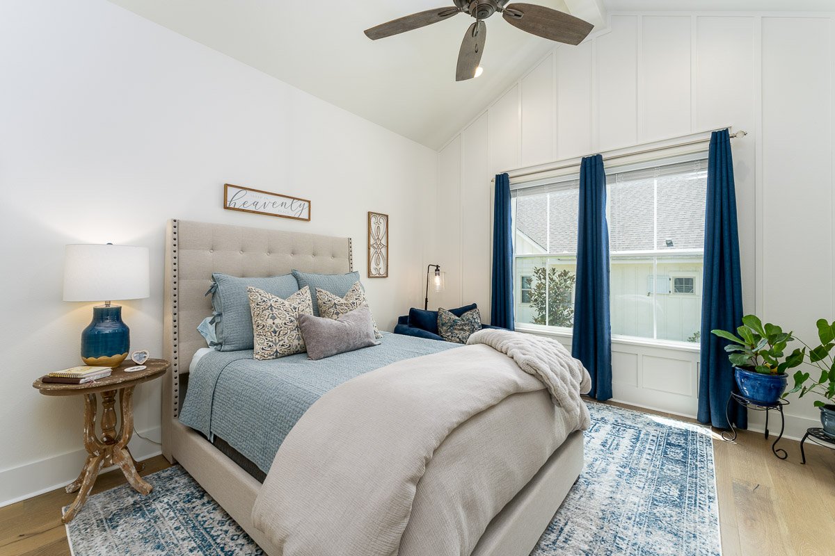 Professional flambient real estate photography of a bright Seattle bedroom with vaulted ceilings, modern staging, blue accents, a large window, and natural light.