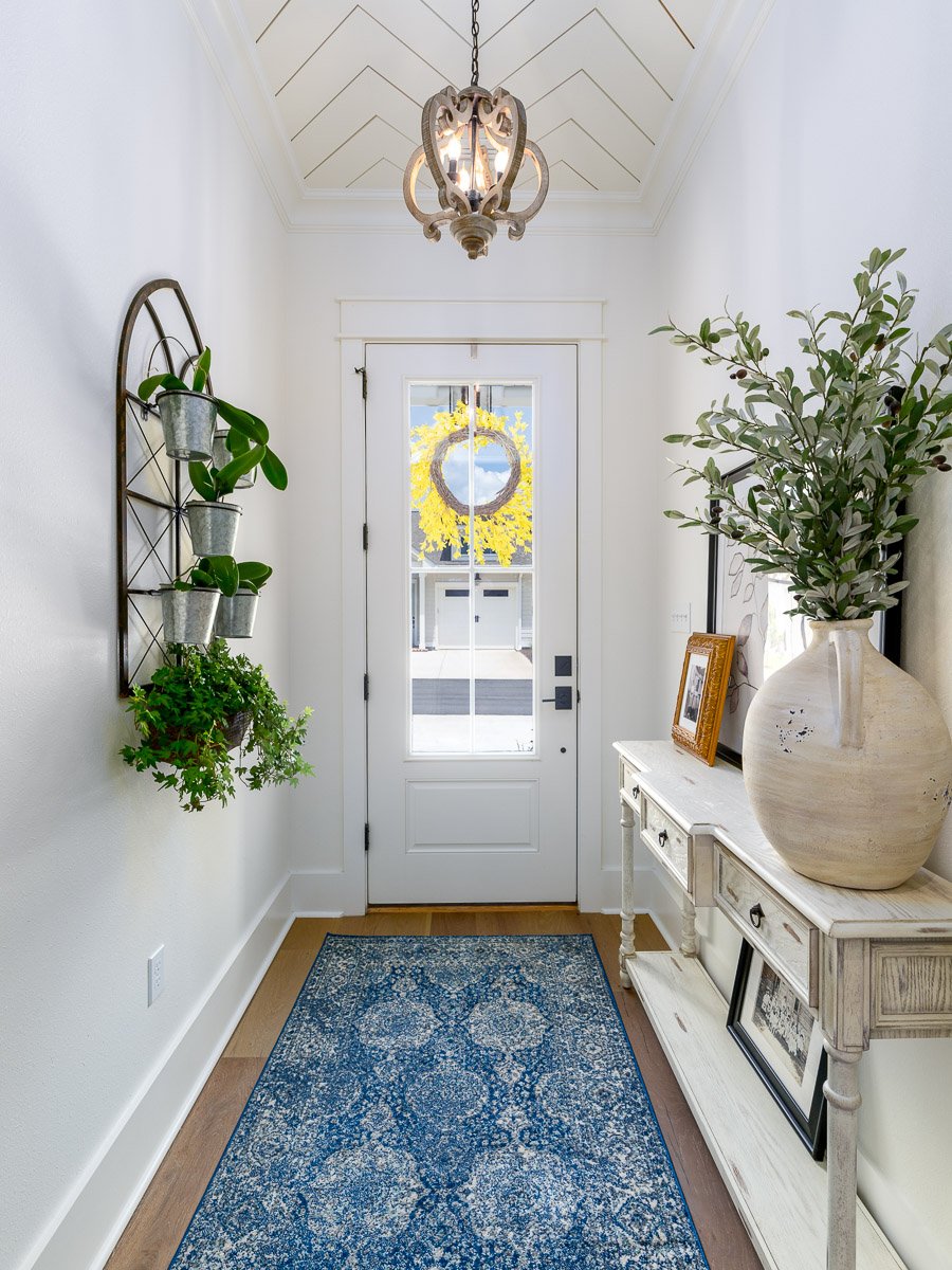 Professional real estate photography of a bright Seattle entryway with a glass front door, decorative ceiling detail, statement chandelier, hardwood floors, and stylish staging.