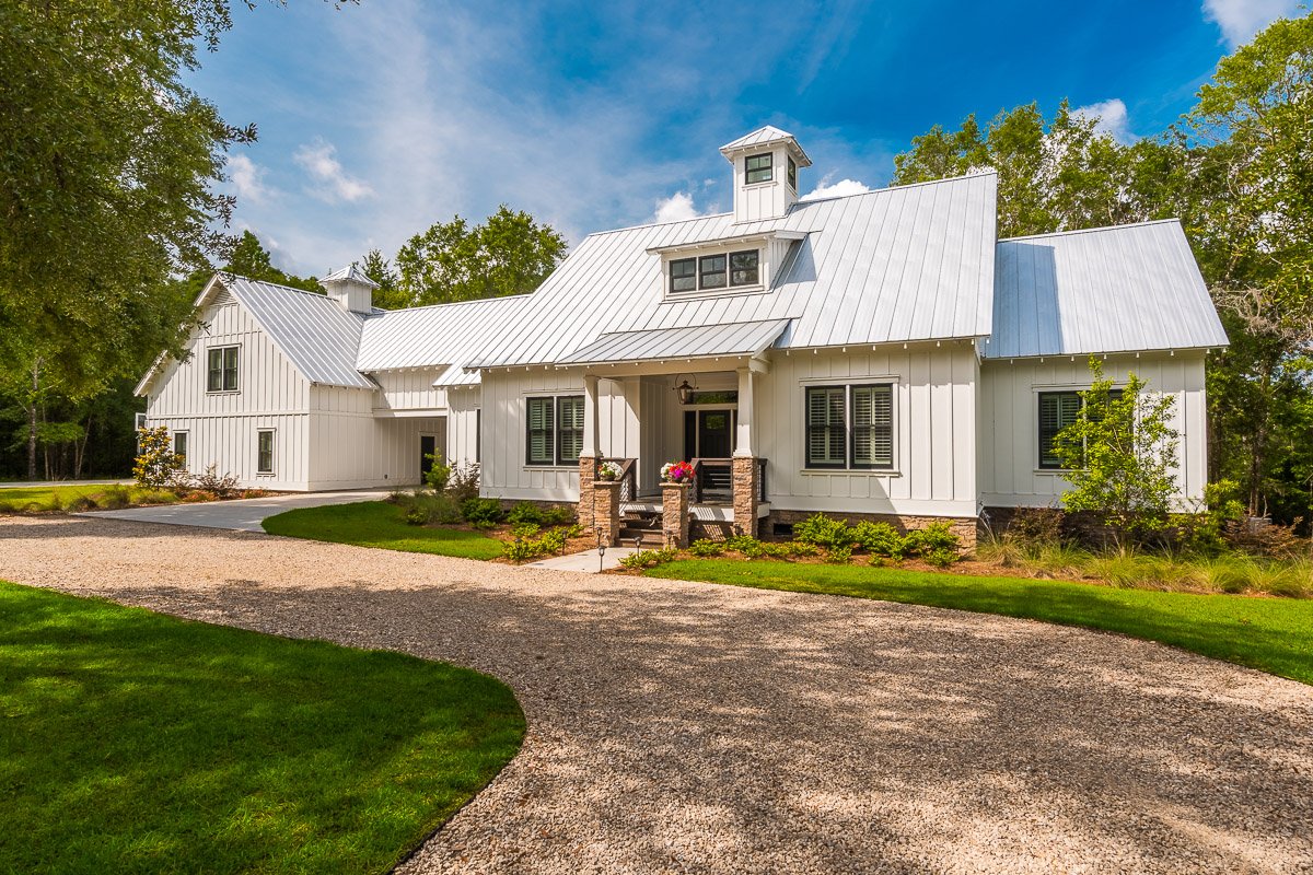 Professional real estate exterior photography of a luxury modern farmhouse-style home with a metal roof, landscaped grounds, and strong curb appeal.
