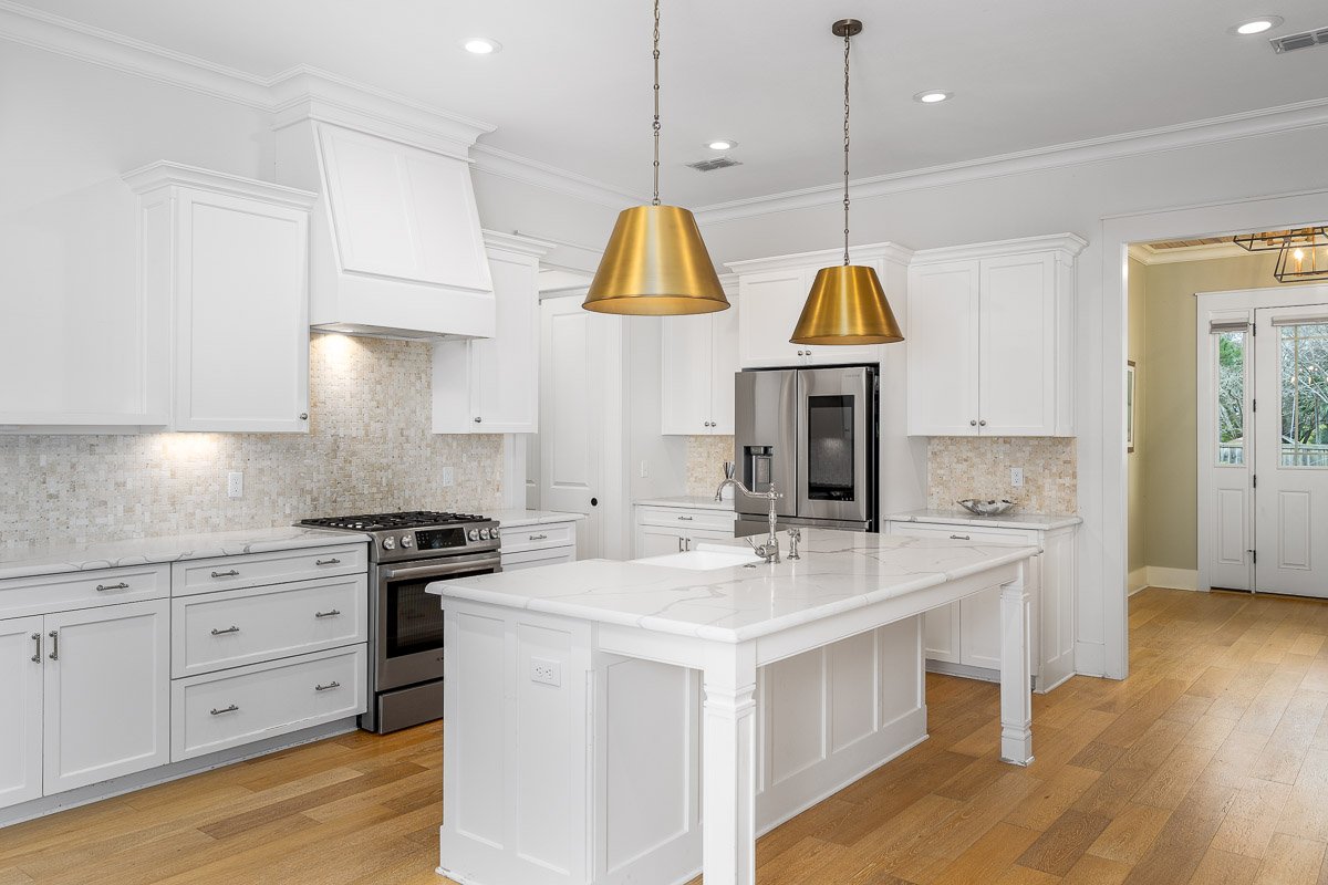 Professional flambient real estate photography of a bright Seattle kitchen with white cabinetry, a large island, brass pendant lighting, stainless steel appliances, and hardwood floors.