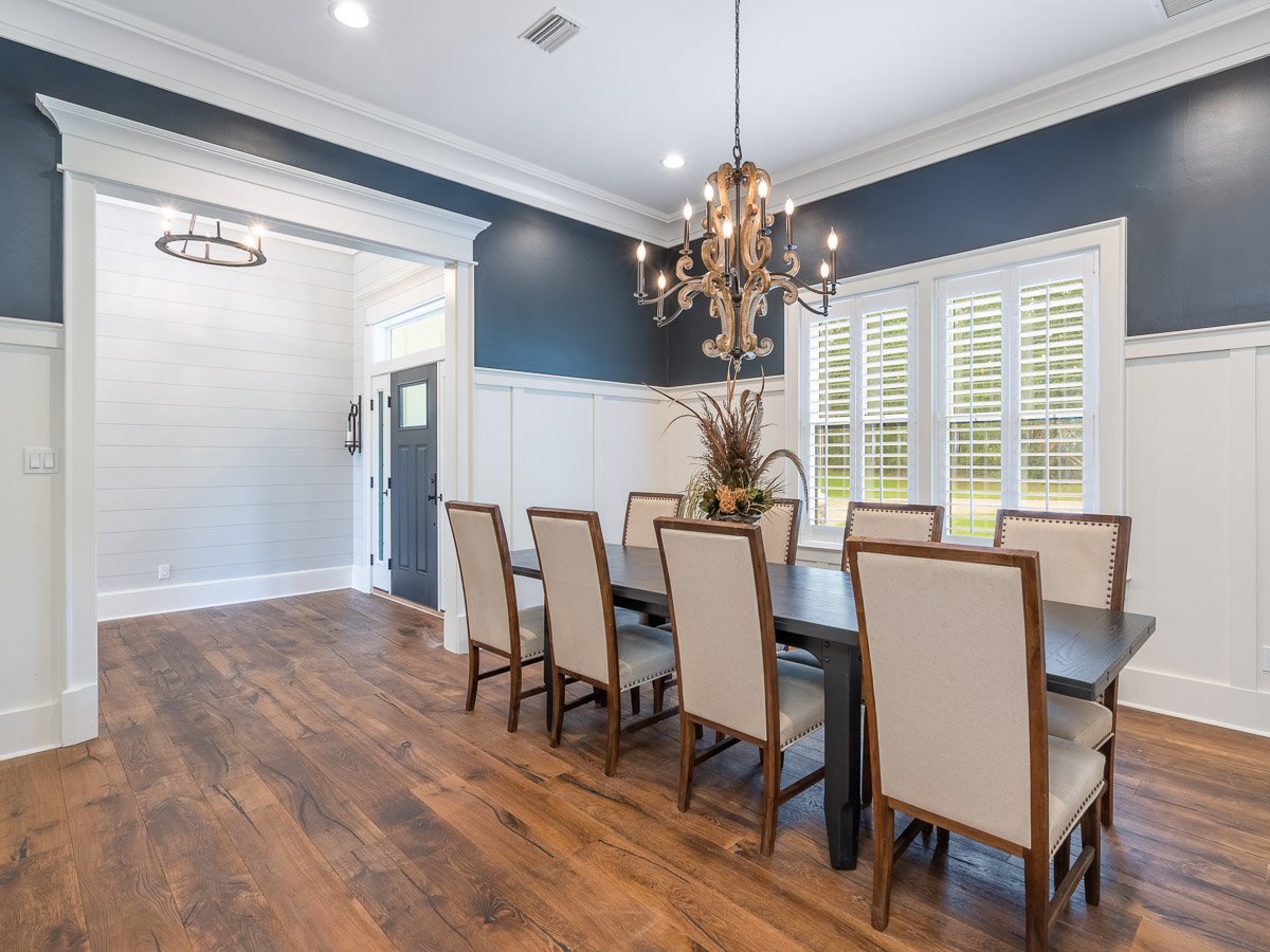 Professional real estate photography of an elegant Seattle dining room with dark blue walls, white wainscoting, hardwood floors, plantation shutters, and a statement chandelier.