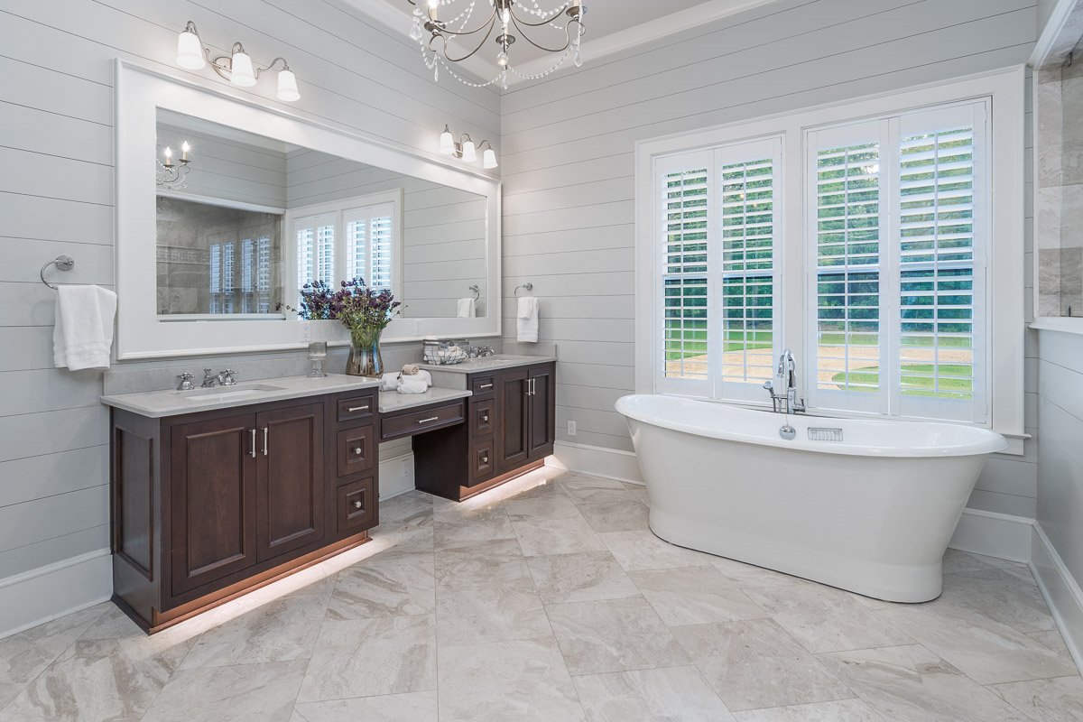 Professional real estate photography of a luxury Seattle bathroom with a freestanding soaking tub, dual vanities, plantation shutters, large mirror, and elegant tile finishes.