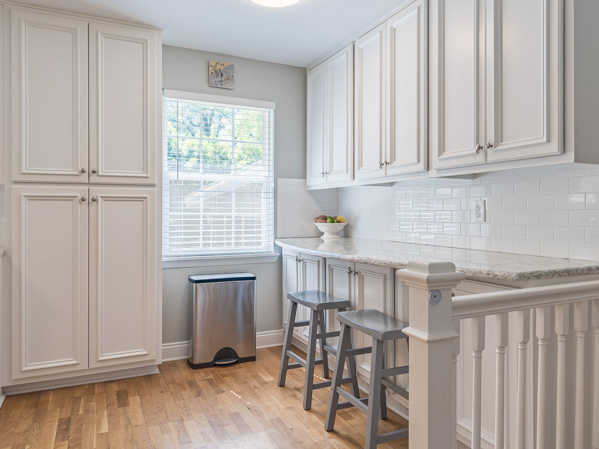 Professional real estate photography of a bright Seattle butler’s pantry with white cabinetry, granite countertops, subway tile backsplash, hardwood floors, and built-in storage.
