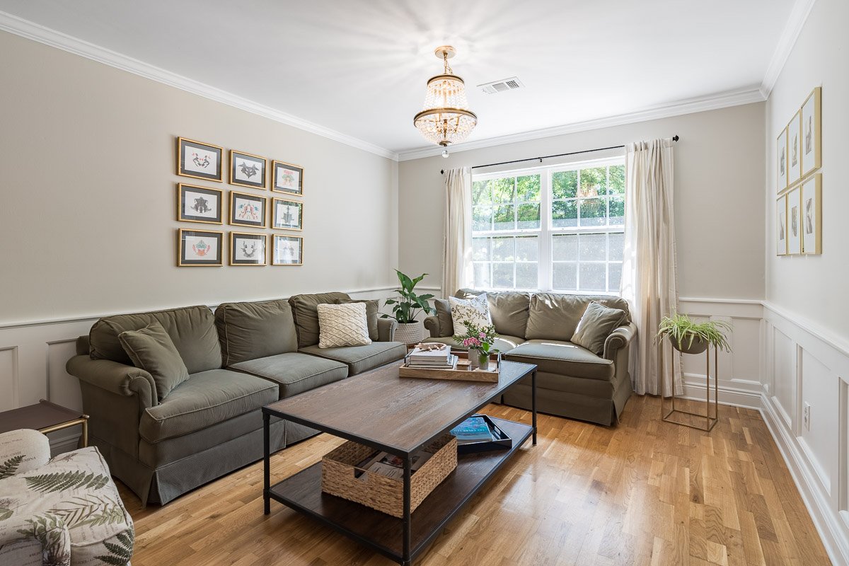 Professional real estate photography of a bright Seattle living room with hardwood floors, classic wainscoting, large windows, traditional chandelier, and comfortable staging.