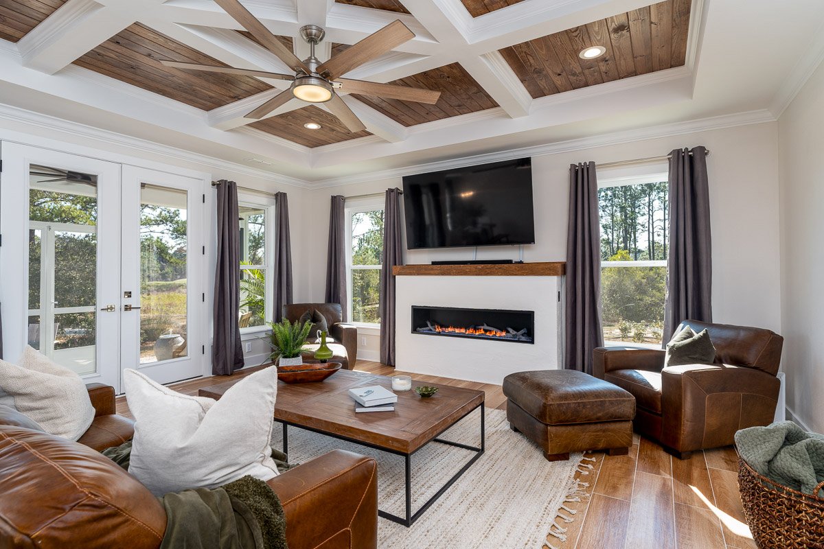 Professional flambient real estate photography of a warm, inviting living room with a custom wood coffered ceiling, modern fireplace, leather seating, and abundant natural light.