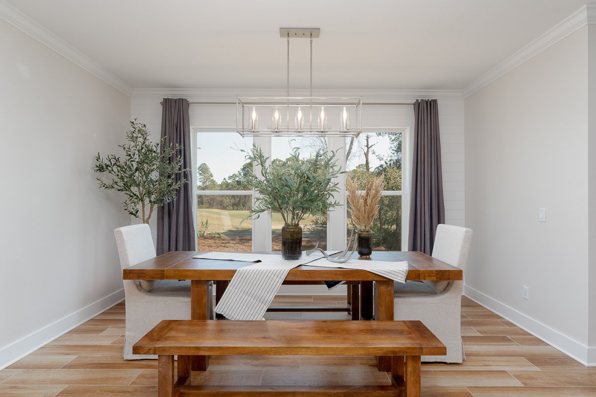 Professional flambient real estate photography of a bright Seattle dining room with a wood table and bench, modern chandelier, large windows, and clean contemporary styling.